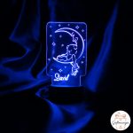 Personalizirana akrilna noćna lampa s imenom i slatkim motivom medvjedića koji spava na mjesecu. Lampa svijetli plavom bojom.