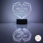 Personalizirana LED lampa u obliku geometrijskog srca koja svijetli bijelim svjetlom, s laserski ugraviranim imenima "Matej & Laura", datumom "10.11.2024." i posvetom "Zauvijek ti i ja", na crnom postolju s odrazom na površini – savršen romantični poklon za parove, Valentinovo i godišnjice.