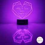 Personalizirana LED lampa u obliku geometrijskog srca koja svijetli bijelim svjetlom, s laserski ugraviranim imenima "Matej & Laura", datumom "10.11.2024." i posvetom "Zauvijek ti i ja", na crnom postolju s odrazom na površini – savršen romantični poklon za parove, Valentinovo i godišnjice.