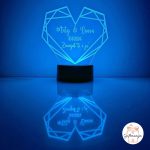 Personalizirana LED lampa u obliku geometrijskog srca koja svijetli bijelim svjetlom, s laserski ugraviranim imenima "Matej & Laura", datumom "10.11.2024." i posvetom "Zauvijek ti i ja", na crnom postolju s odrazom na površini – savršen romantični poklon za parove, Valentinovo i godišnjice.