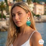 Portret mlade žene s dugom plavom kosom i zelenkastim očima koja nosi upečatljive naušnice. Naušnice se sastoje od zlatnog gornjeg dijela, bijelog detalja u obliku srca i velikog donjeg dijela od tirkizno-zelenog zrcalnog akrila u obliku lista monstere. Djevojka nosi ljetnu bijelu majicu na tanke naramenice, a u pozadini se nazire blago zamućeni pejzaž mora i obalnog grada Opatije.